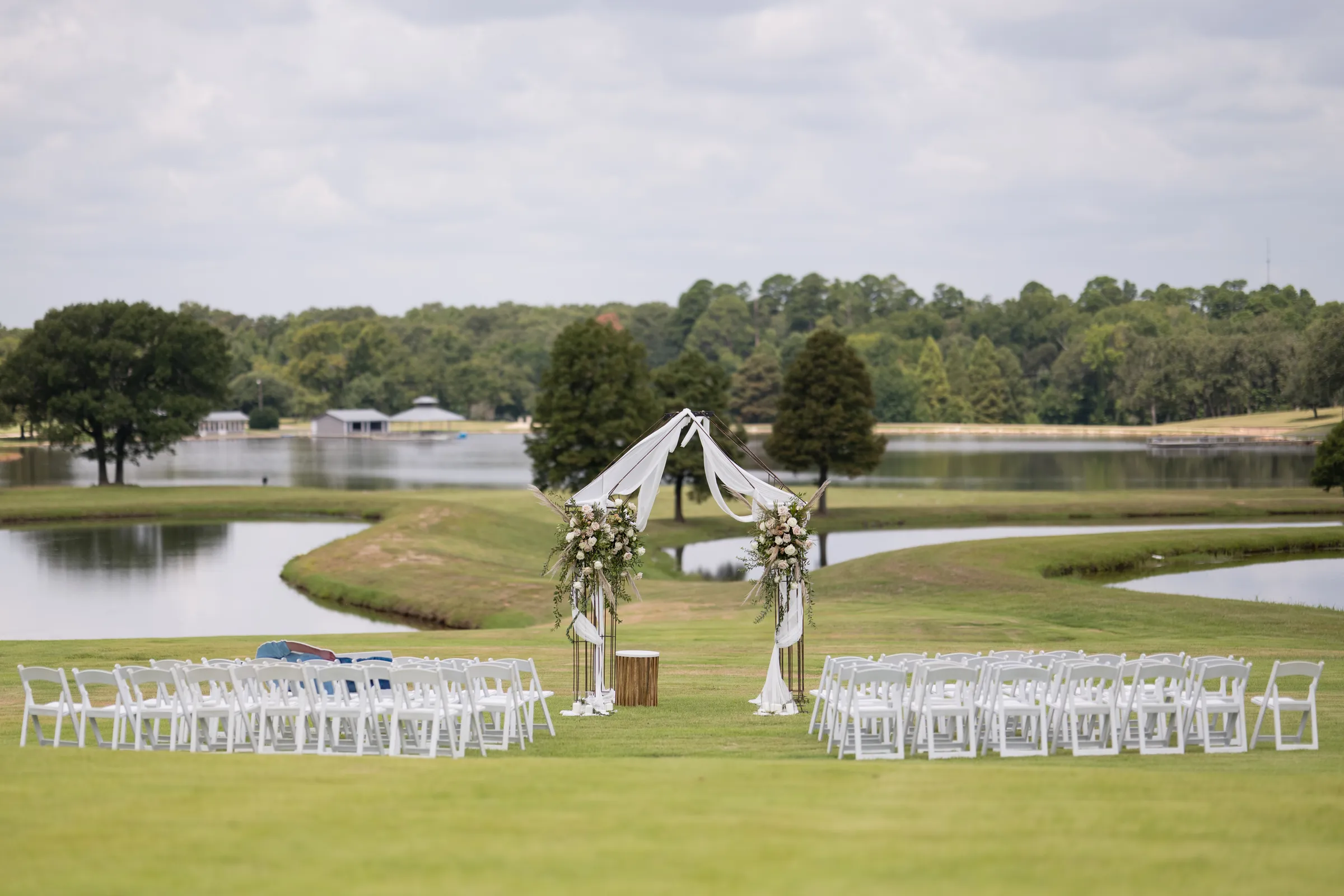 White chairs and a floral arch set for a ceremony on the lawn by the lake at Pine Cone Ranch